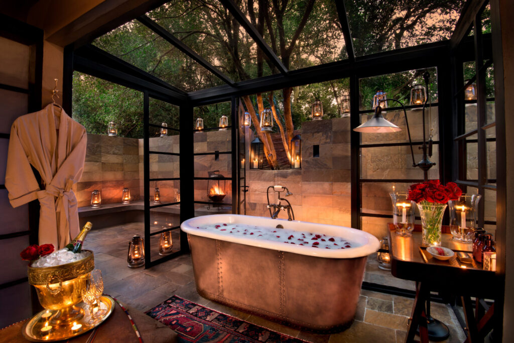 Luxury copper bathtub decorated with rose petals and candlelight, set for a romantic safari couple’s retreat in Africa.